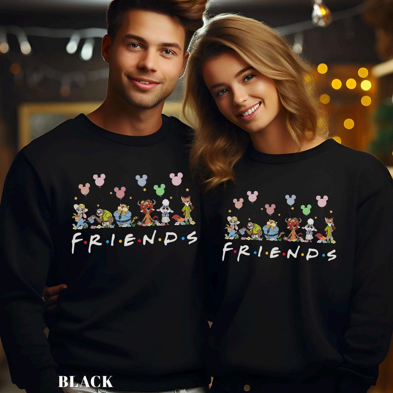 Pode incluir: Camisolas pretas com um design de desenho animado com personagens da Disney e a palavra "FRIENDS" em branco. O design inclui orelhas do Mickey Mouse e v&aacute;rias figuras de desenhos animados. Usadas por duas pessoas.