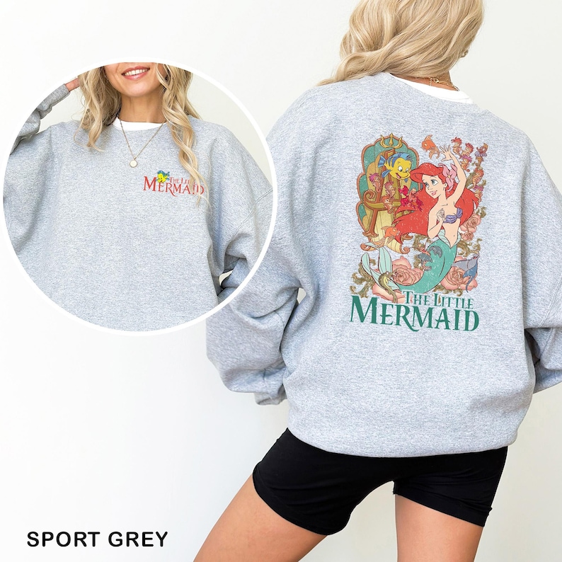 以下が含まれることがあります： スポーツグレーのスウェットシャツ。背中には、リトルマーメイドのアリエル、フランダー、セバスチャンのカラフルなグラフィックが描かれています。スウェットシャツの前面には、赤と黄色で「The Little Mermaid」の文字がプリントされています。クルーネックのスウェットシャツです。