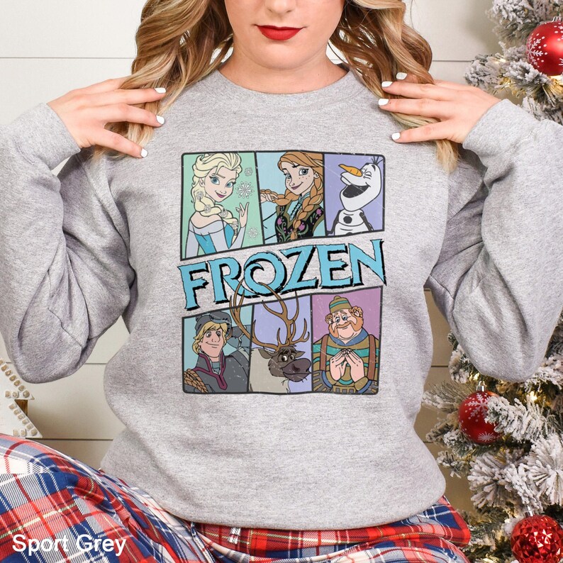 Puede incluir: Una sudadera gris claro con un gr&aacute;fico colorido de personajes de la pel&iacute;cula "Frozen". La palabra "FROZEN" est&aacute; impresa en azul y blanco. La sudadera est&aacute; hecha de un material suave.