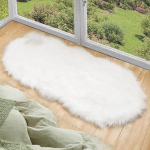 Puede incluir: Una alfombra ovalada blanca y esponjosa con fibras largas. La alfombra está sobre un suelo de madera.