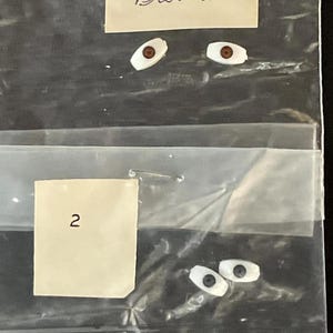 May include: Two pairs of doll eyes, one pair brown and one pair blue. The brown eyes are in a plastic bag with a label that says "Brown". The blue eyes are in a plastic bag with a label that says "2".