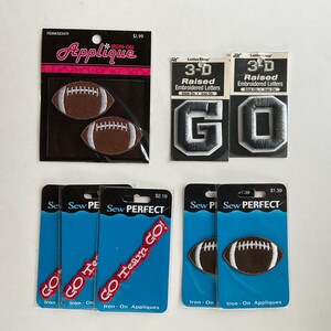 May include: A set of iron-on appliques featuring footballs and the words "GO Team GO!" and "GO". The appliques are on white cards with blue and red text.