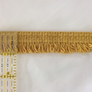 May include: A close-up of a yellow fringe trim measured with a ruler. The fringe is about 1 inch wide.