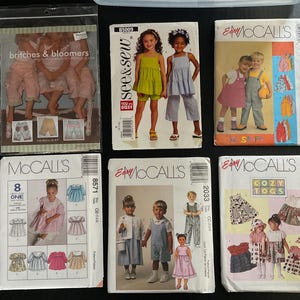 May include: A collection of children's sewing patterns, featuring various designs for clothing such as dresses, overalls, and bloomers. The patterns are from brands like McCall's and See & Sew, with images of the finished garments.