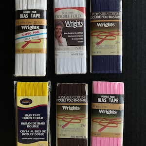 May include: Six packages of double fold bias tape in various colors, including white, navy, yellow, brown, and pink. Each package features the Wrights brand logo and includes the length, color, and product number. The packages are arranged in two rows of three.