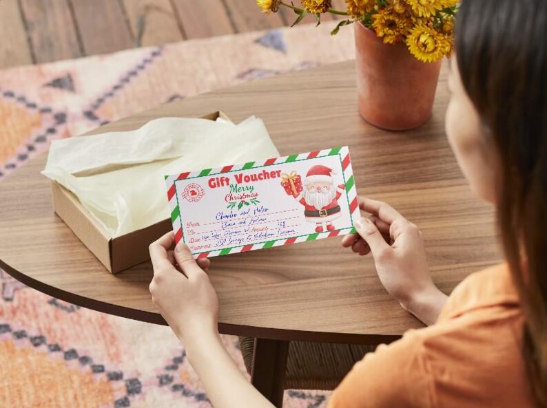 Puede incluir: Un vale de regalo rojo y verde con un Pap&aacute; Noel de dibujos animados sosteniendo un regalo. El vale dice "Vale de regalo Feliz Navidad" y tiene un espacio para el nombre del destinatario y una lista de regalos.