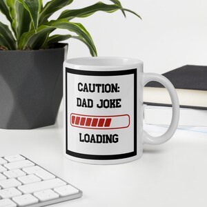 May include: White ceramic mug with a black border and the text "CAUTION: DAD JOKE LOADING" in black and red. The progress bar is red and almost full.