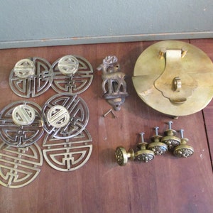 May include: A collection of brass hardware, including door knobs, drawer pulls, and a decorative door knocker. The hardware features a traditional Chinese design with a circular shape and intricate details. The door knocker is shaped like a deer and has a ring for pulling.