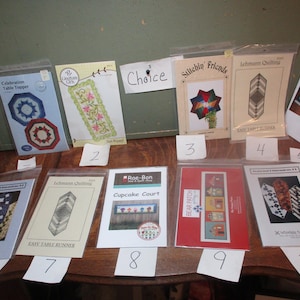 May include: A collection of 10 quilting patterns, each with a different design and title. The patterns are displayed on a wooden table with numbered labels.