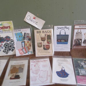May include: A collection of 10 quilting patterns for bags, coasters, and aprons. The patterns are printed on white paper with colorful illustrations and text. The patterns include titles like "BB Bags", "Tech Cover", "Screen Play", and "Childhood Frolics".