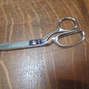 May include: Silver sewing shears with a black handle and the word "SINGER" printed on the blade.