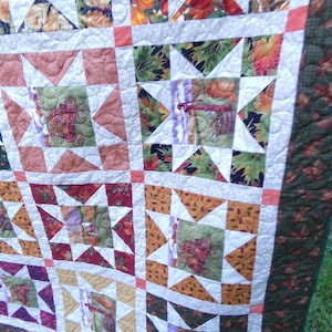 May include: A handmade quilt with a patchwork design. The quilt features squares with star patterns in shades of orange, green, red, and purple, bordered by white and a green leaf pattern. The quilt is likely for a bed or a decorative throw.