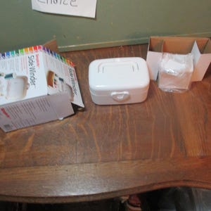 May include: A white plastic storage box with a heart-shaped latch. The box is labeled "Side Winder" and is sitting on a wooden table.