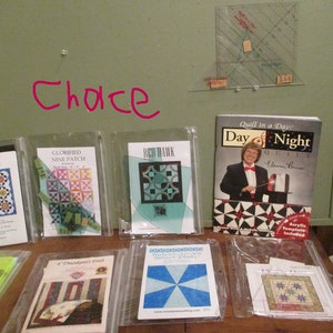 May include: A collection of quilting patterns and a book titled "Quilt in a Day: Day & Night Quilt" by Eleanor Burns. The patterns include "Stack-n-Whack 45° Triangle Tool", "Glorified Nine Patch", "Red Hawk", "A Thousand's Ruff", "Small Plate", and "Starry Night".