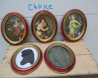 May include: Five oval-shaped picture frames with gold and red trim. The frames are arranged in a row on a light wood surface. The frames contain various images, including a silhouette of a person's head, a portrait of two women, and a portrait of a young girl.