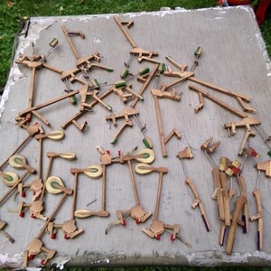 May include: A collection of disassembled piano parts, including wooden hammers, levers, and dampers, scattered on a weathered gray surface. The parts have various colors, including natural wood, green, red, and silver metal components.