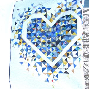 May include: A white quilt with a blue and yellow heart design made of patchwork triangles. The quilt is hanging on a clothesline.