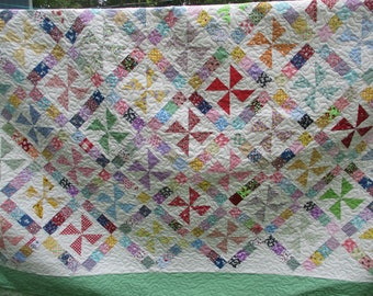 May include: A white quilt with a green border. The quilt is made up of many small squares of different colors and patterns. The squares are arranged in a repeating pattern of pinwheels.