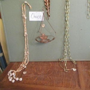 May include: A display of decorative items, including a beaded necklace, a hanging planter, and a chain with a circular base. The items are displayed against a green background. A sign that says "Choice" is also visible.
