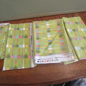 May include: Four pieces of green fabric with a pattern of colorful kitchen utensils. The fabric is labeled "Pink Piglet Everything Nice" and "Green Print Dt 12837".