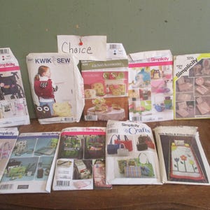 May include: A collection of 11 sewing patterns for various crafts and projects, including kitchen accessories, bags, and quilts. The patterns are from Simplicity and Kwik Sew brands.