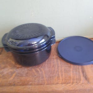 May include: A dark blue, round cooking pot with a matching lid. The pot has two handles and a vented top. The lid is flat and circular. The items are on a wooden surface.