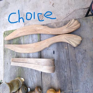 May include: Wooden furniture components, including two curved, carved pieces with a fan-like design, a rectangular piece, and several turned wooden pieces. The word "choice" is written in blue marker.