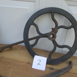 May include: A dark gray, cast iron wheel with a series of curved spokes and a central hub. A long, thin arm extends from the wheel's edge. A small piece of paper with the number "2" is visible.