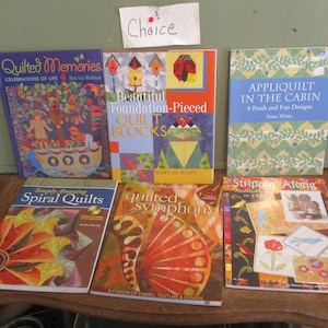 May include: A collection of quilting books with colorful covers featuring various quilting designs and titles such as "Quilted Memories", "Beautiful Foundation-Pieced Quilt Blocks", "Appliquilted in the Cabin", "Spiral Quilts", "Quilted Symphony", and "Strippin' Along".
