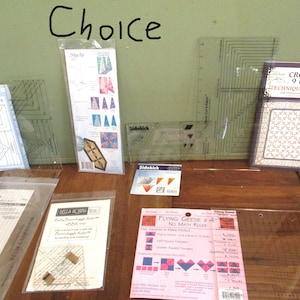 May include: A collection of quilting rulers and templates, including square, rectangular, and specialty shapes. The image features clear plastic rulers with grid markings, packaged with instructions. The word "Choice" is written in black marker on the wall.