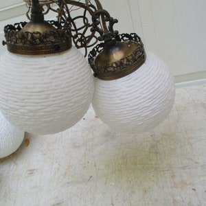 May include: Vintage chandelier featuring three white globe-shaped lamps with a textured surface. Each lamp has a decorative brass-colored crown. The lamps are suspended from a decorative metal fixture.