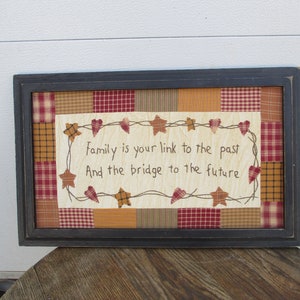 May include: Framed wall art with a patchwork design in red, gold, and brown. The central panel features the quote, "Family is your link to the past And the bridge to the future," framed with stars and hearts.