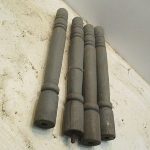 May include: Four gray wooden furniture legs with a turned design. The legs are cylindrical with decorative rings near the top and bottom. The wood has a weathered appearance.