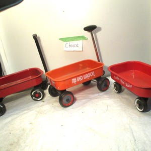May include: Three red toy wagons with black wheels and handles. One wagon has the text "My Red Wagon", and another has "Little Red Racer". The wagons are on a white surface.