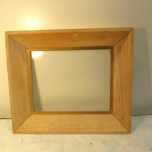 May include: A simple wooden picture frame with a gold-colored mat and glass. The frame is light brown and has a natural wood grain.