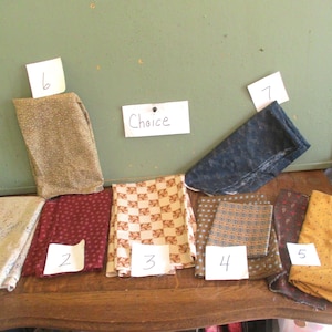 May include: A selection of fabric swatches in various colors and patterns, including floral, polka dot, and geometric designs. The swatches are numbered and displayed on a wooden surface. The word "Choice" is written on a white paper.