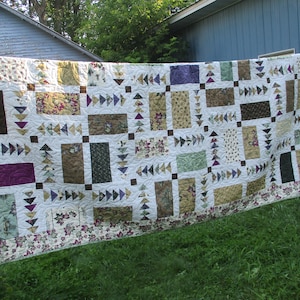 May include: A patchwork quilt with a white background and various colored squares and rectangles. The quilt features a pattern of small, white triangles with brown borders. The quilt is hanging on a clothesline.