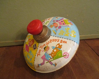 Könnte beinhalten: Ein vintage Kreisel aus Metall mit bunten Illustrationen von Kinderreimfiguren, darunter Old King Cole, Tom Tom the Piper's Son und Mary Had a Little Lamb. Das Spielzeug hat einen leuchtend roten Kunststoffgriff und einen Metallsockel.