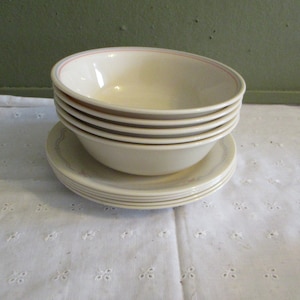 May include: A stack of six white ceramic bowls with a light blue and pink trim. The bowls are nested together and have a floral design on the bottom.
