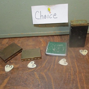 May include: Five vintage metal boxes with a green, silver, and brass finish. The boxes are arranged on a wooden surface with five heart-shaped tags labeled with numbers 01, 02, 03, 04, and 05.