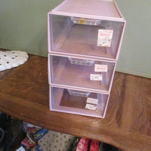 May include: Three stackable clear plastic drawers with a light pink lid. The drawers are labeled "Sterilite" and have a price tag on the top drawer.