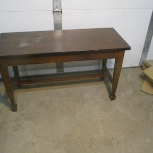May include: A rectangular wooden table with a dark brown top and lighter brown legs. The table has a lower shelf and is approximately 36 inches long, 20 inches wide, and 30 inches tall. The table is made of wood and has a simple, classic design.