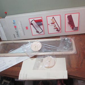 May include: A white plastic, three-way corner shelf with a mirror. The shelf is packaged in a box with the words "Living Home" and "Three-Way Corner Shelf" printed on it.