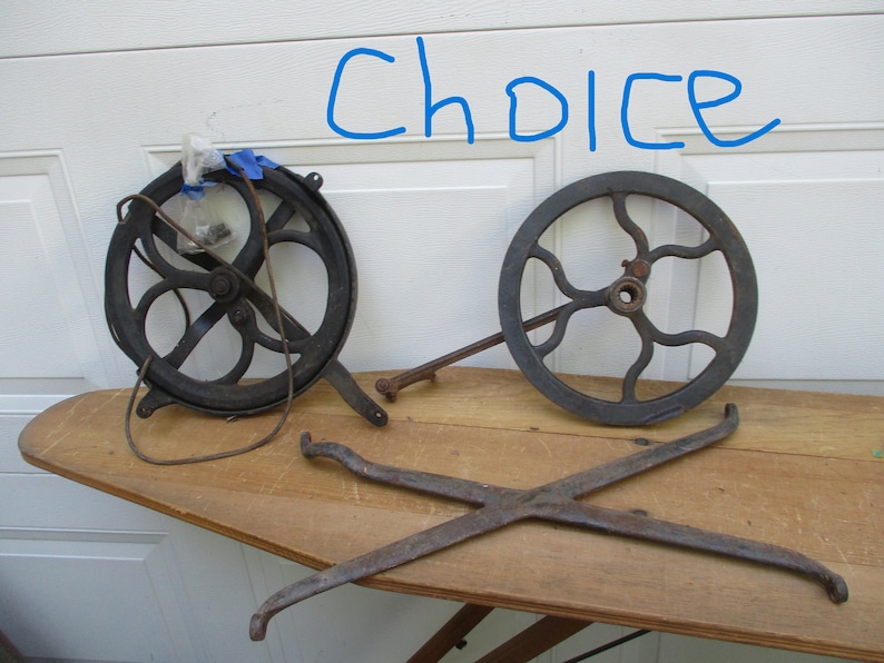 May include: An assortment of antique metal parts, including two spoked wheels and a cross-shaped piece, arranged on a wooden surface. The word "Choice" is written in blue marker above the objects.