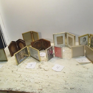 May include: A collection of ten gold-toned picture frames with various sizes and styles. Some frames have photos inside, while others are empty. The frames are arranged on a white surface.
