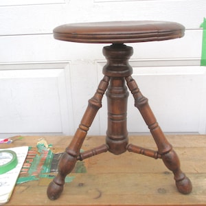May include: A wooden stool with a round seat and three legs. The stool is made of dark wood and has a simple design.