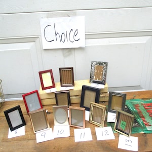 May include: A collection of 13 different picture frames, numbered 1 through 13, arranged on a wooden surface. The frames are made of various materials, including wood, metal, and plastic. The frames are all different sizes and shapes. The word "Choice" is written on a white piece of paper above the frames.
