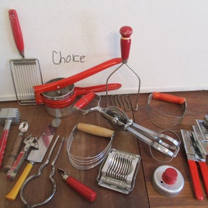 May include: A collection of vintage kitchen utensils with red handles, including a potato masher, egg slicer, and can openers. The tools are arranged on a wooden surface, showcasing a retro aesthetic.