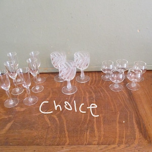 May include: A collection of clear glass cordial and shot glasses. The glasses vary in size and design, with some featuring intricate patterns. The word "Choice" is written in white cursive on the wooden surface.