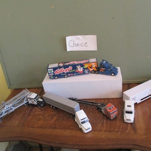 May include: A collection of toy semi-trucks and trailers in various colors and designs. Includes a blue and white Kellogg's truck, a white trailer with blue accents, and other miniature vehicles.